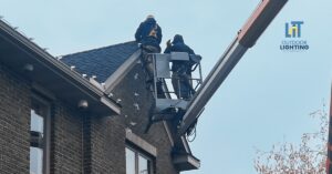 Electrician holding holiday lights near a home